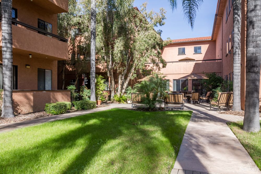 Sunny courtyard of an apartment complex with a well-maintained green lawn and surrounding trees.
