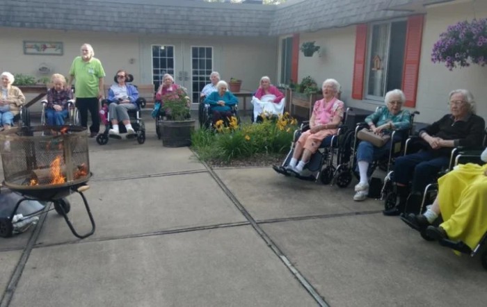 A group of elderly individuals sitting outdoors in wheelchairs, enjoying a peaceful day in the garden of a nursing home.