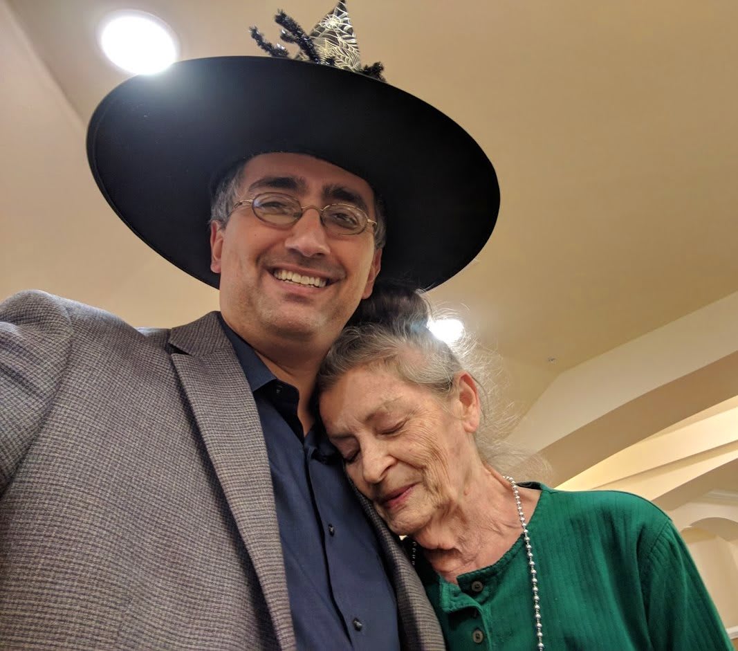 A man wearing a hat is smiling while a woman rests her head on his shoulder.