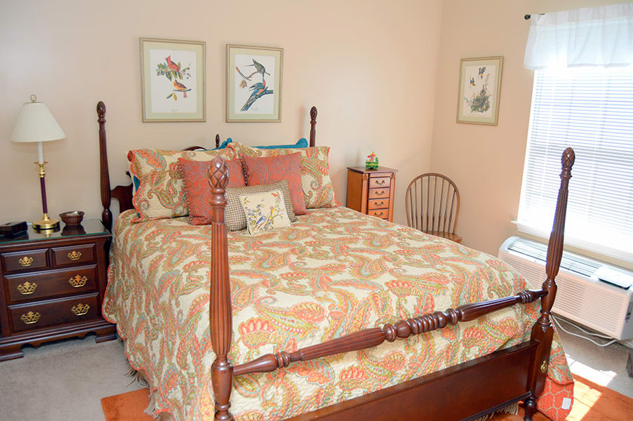 A cozy bedroom featuring a wooden four-post bed with floral bedding and coordinating pillows, complemented by framed botanical artwork on the walls.