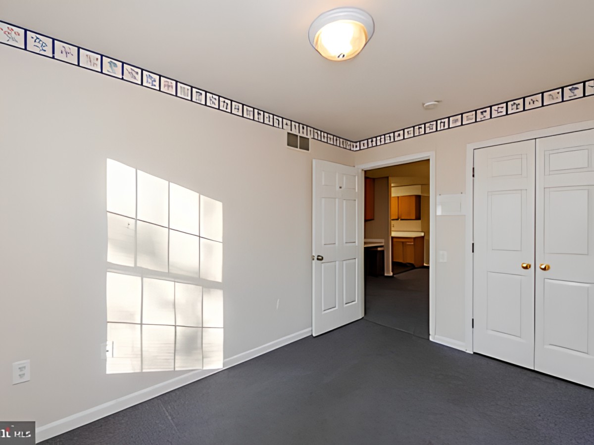 An empty room with carpet flooring, a window casting light, and a door leading to another area.