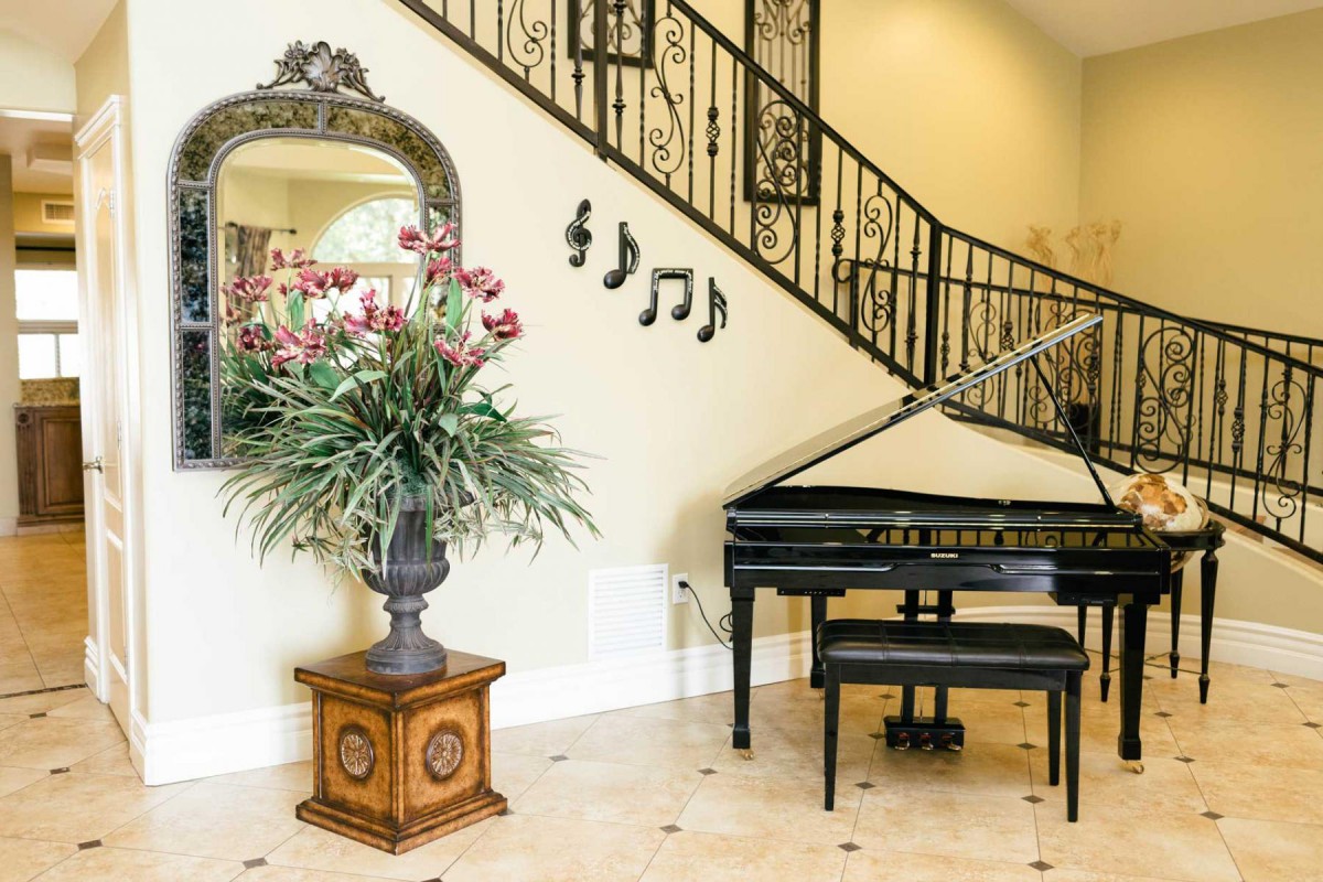 A luxurious living area featuring a grand piano, a decorative plant, and intricate staircase railing.