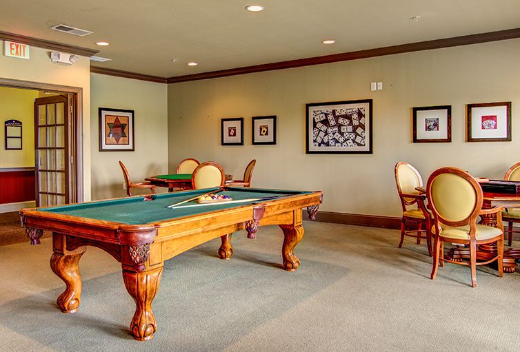 A recreational room featuring a pool table, surrounded by chairs and decorated with framed photographs on the walls.