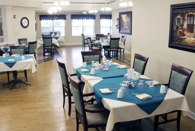 A dining room with neatly arranged tables and chairs, featuring blue tablecloths and a well-lit setting.