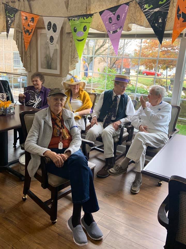 A group of seniors sitting indoors, wearing various hats and surrounded by festive decorations.