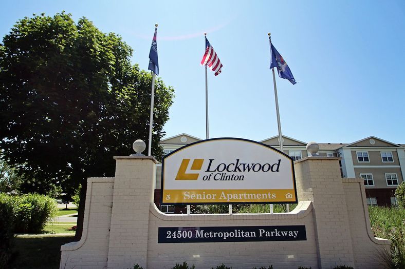 The entrance sign for Lockwood of Clinton, featuring three flags on poles and a visible address: 36900 Metropolitan Parkway.