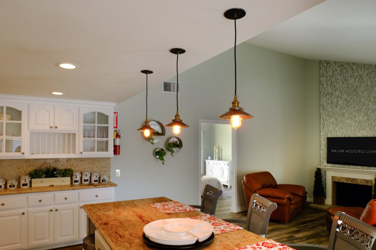 A cozy kitchen interior featuring pendant lights above a wooden table, complemented by chairs and decorative touches like plants.