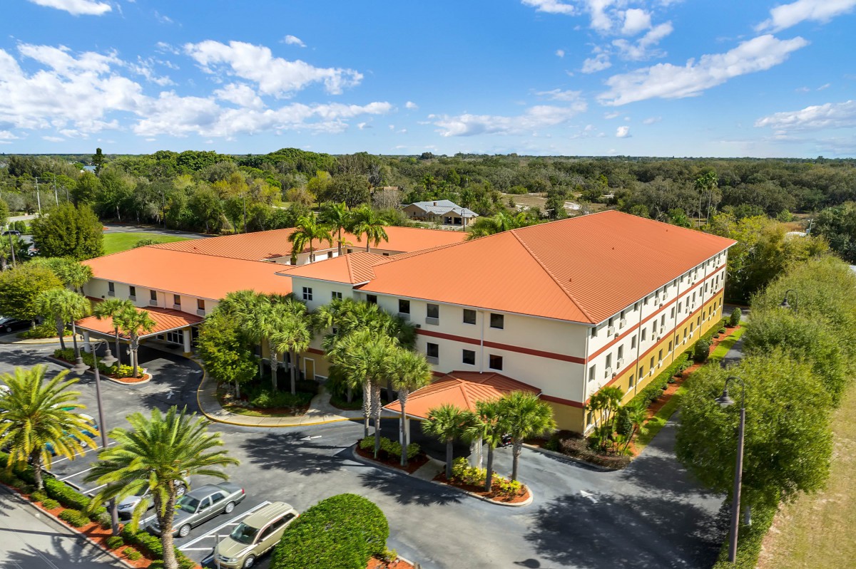 Aerial view of a large building with a red roof surrounded by trees and a parking lot.