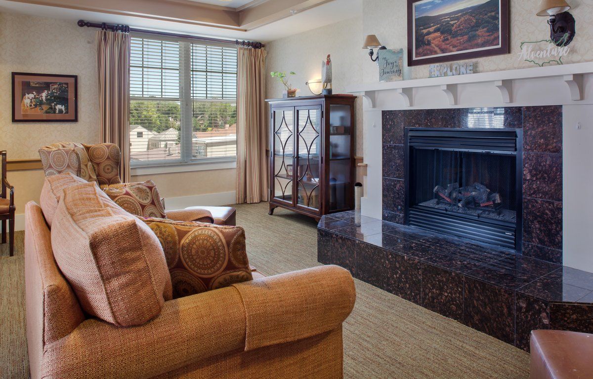 A cozy living room featuring a comfortable sofa and armchair set near a fireplace, with a large window providing natural light.