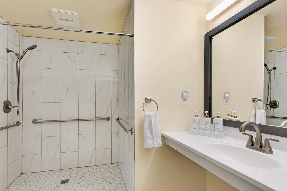 A modern bathroom with a walk-in shower, sink, and mirror.