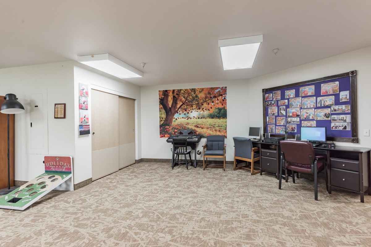 A cozy office waiting area with chairs, a table, computer desk, and a large picture of an autumn tree.