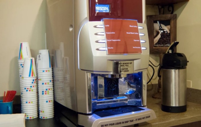 A modern beverage dispenser with multiple options and a stack of cups nearby.