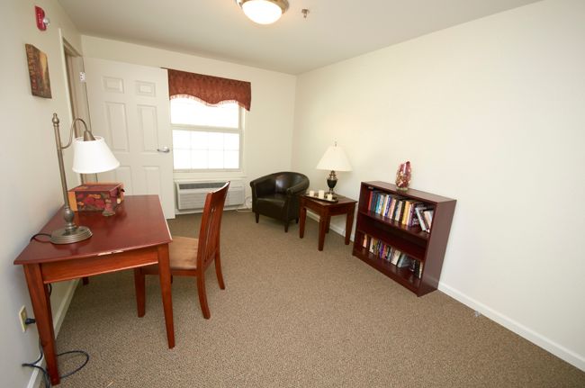 A simple office space with a desk, chair, bookshelf, and lamps.