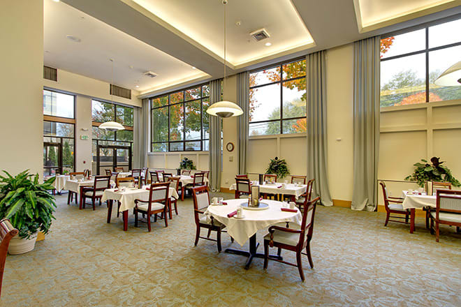 An elegant dining room with neatly arranged tables and chairs, featuring large windows and a spacious atmosphere.