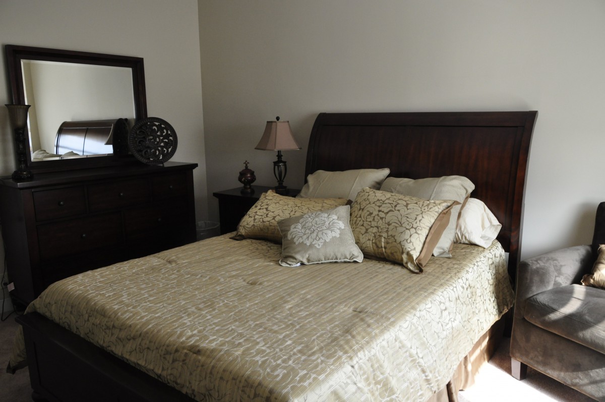 A cozy bedroom with a neatly made bed and decorative pillows, featuring a wooden headboard and matching furniture.