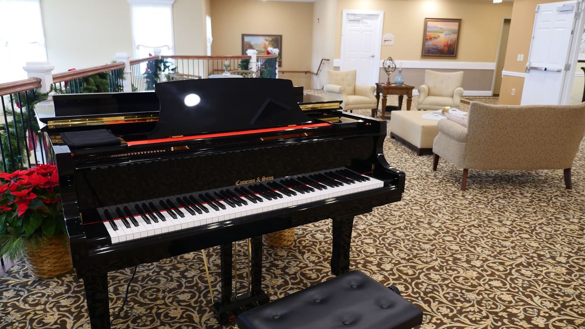 A grand piano in a well-furnished lounge area with carpeted flooring.