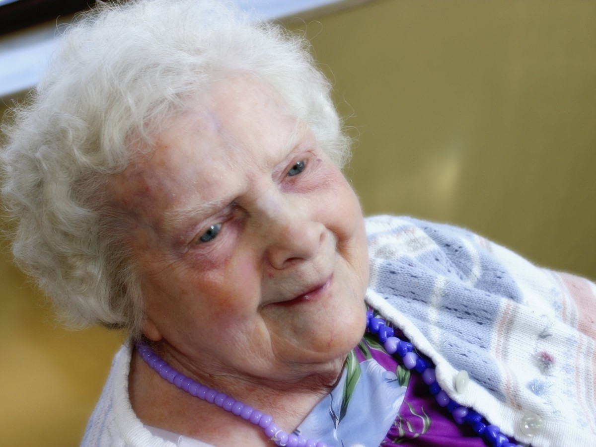 An elderly woman with white hair smiles warmly.