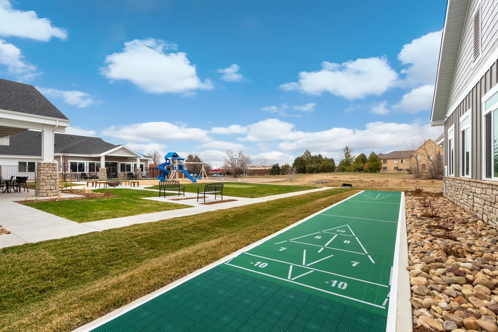 A scenic park featuring a shuffleboard court and playground under a clear blue sky.