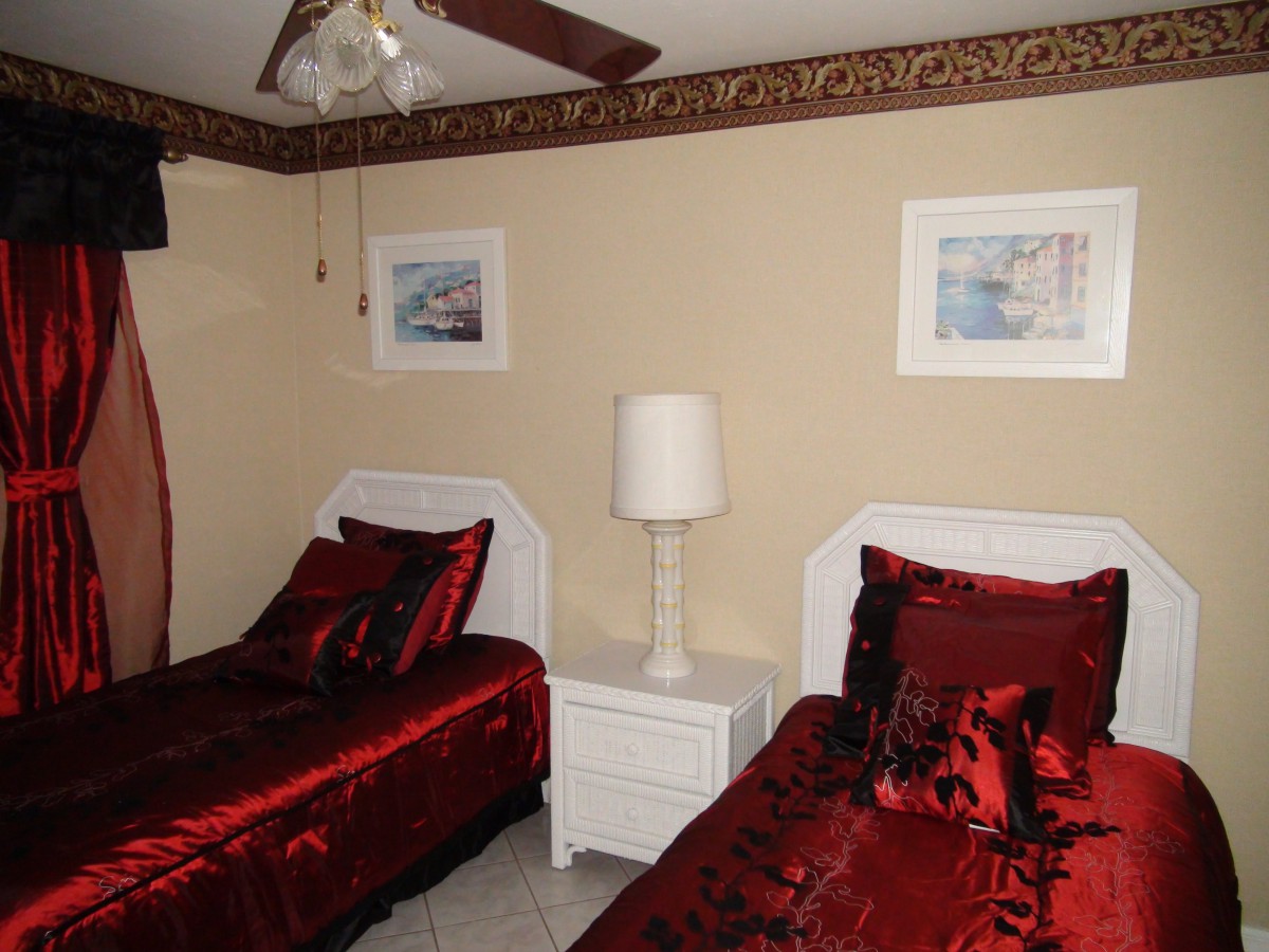 A cozy bedroom features twin beds with luxurious red bedding, a central nightstand with a lamp, and framed artwork on the walls.