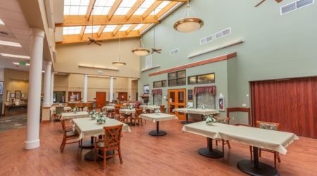 A spacious dining hall with tables and chairs, featuring large skylights and wooden flooring.