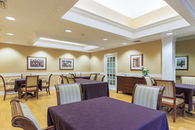 A well-lit dining room with neatly arranged tables and chairs, adorned with framed artwork on the walls.