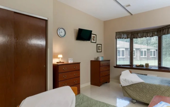 A minimalist bedroom with furniture, including dressers, a wall-mounted television, and a window allowing natural light.