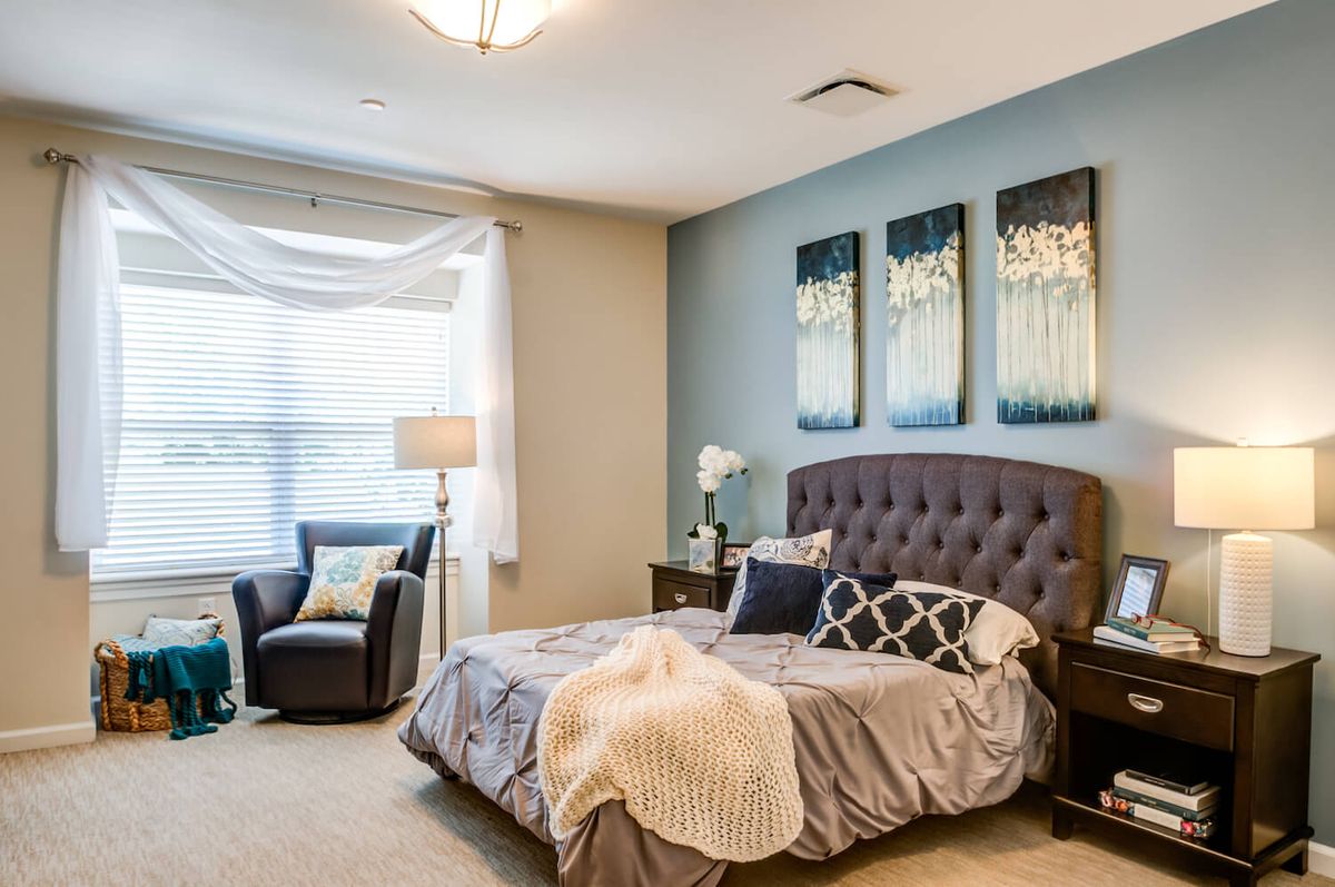 A beautifully decorated bedroom with modern furniture and artwork, featuring a comfortable bed and ample natural light.