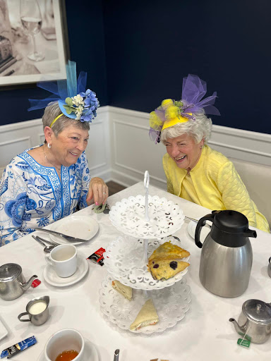 Two joyful friends enjoying an afternoon tea together with colorful hats and delicious treats.