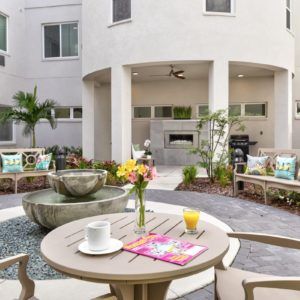 A modern outdoor patio with a fountain, surrounded by comfortable seating and vibrant flowers.