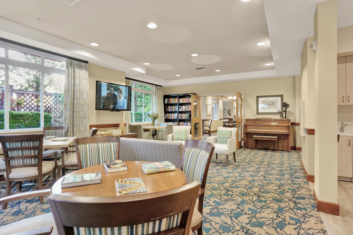 A cozy, well-furnished living room with a piano, bookshelves, and multiple seating areas.