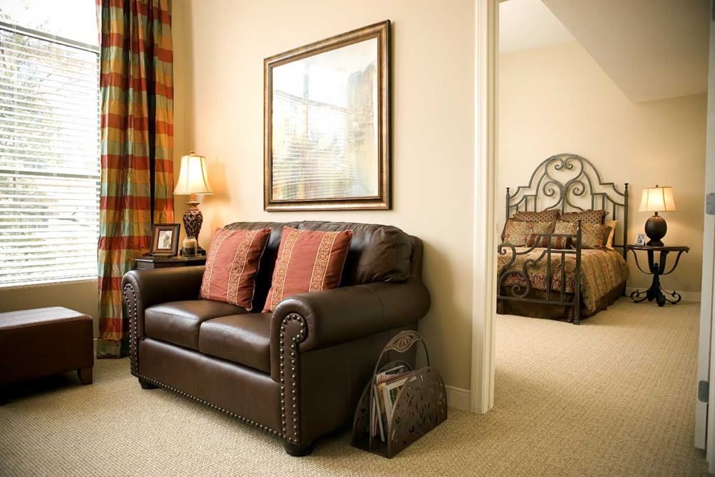 A cozy living room with a leather sofa and cushions, adjacent to a bedroom.