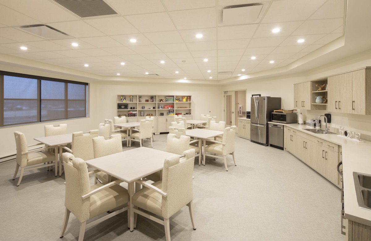 A modern dining area with white tables and chairs, complemented by kitchen appliances.