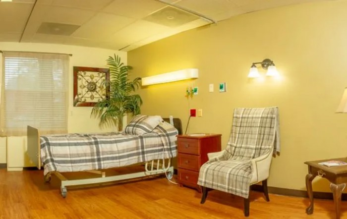 A hospital room featuring a bed, chair, and side table, designed for patient care.