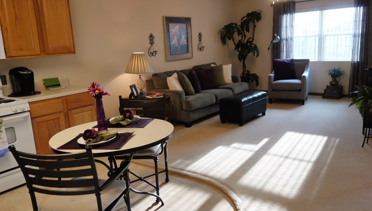 Cozy living room with a sofa, armchair, and dining table, accentuated by warm lighting and indoor plants.