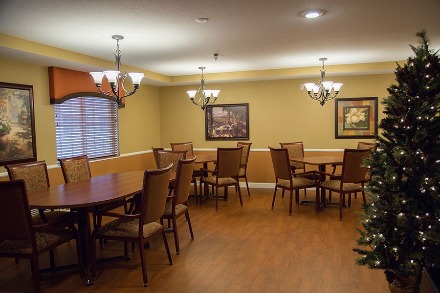 A neatly arranged dining room with several tables and chairs, decorated with chandeliers and artwork on the walls.