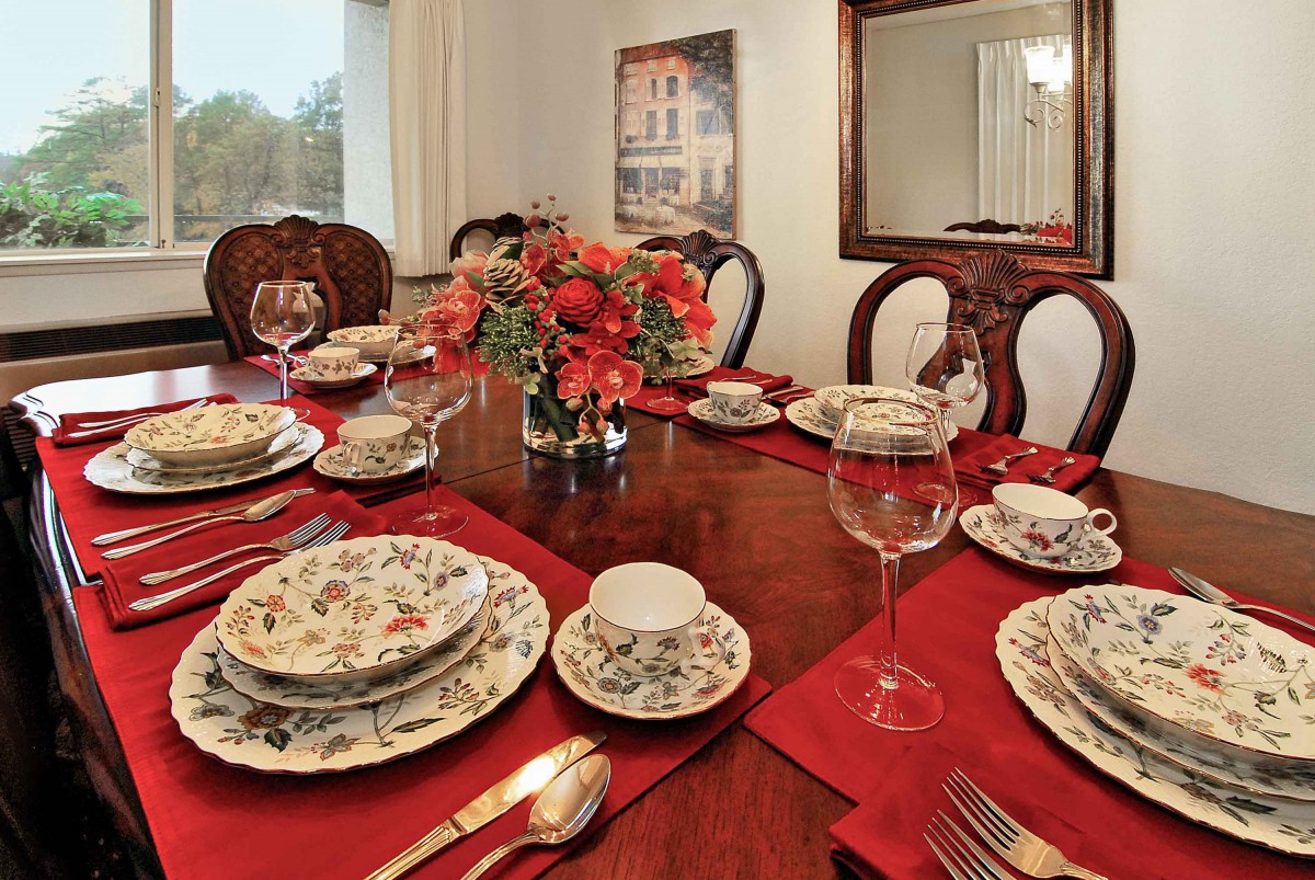 A formal dining table set with patterned dinnerware, red napkins, and a central floral arrangement.
