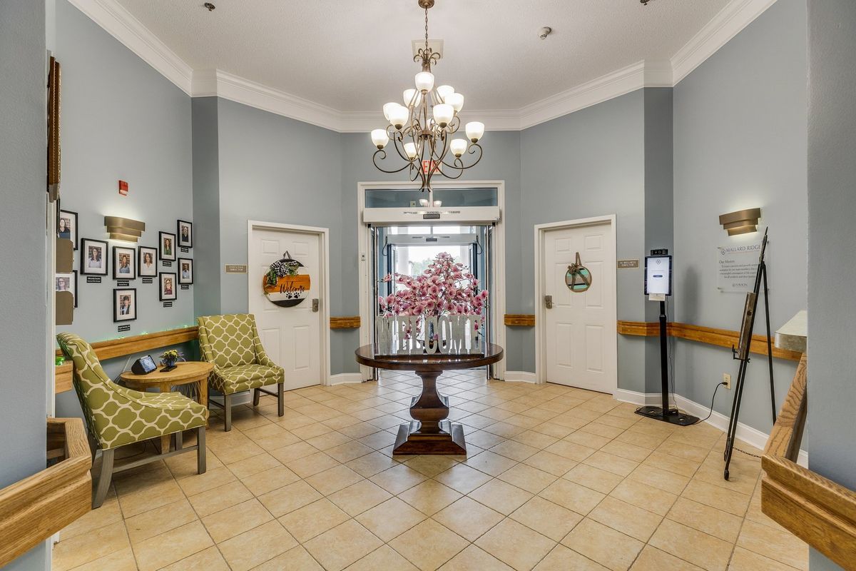 A well-decorated lobby with a central table holding flowers, flanked by chairs, and illuminated by a chandelier.