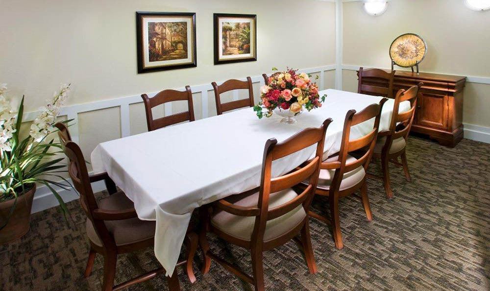 A dining room setup with a white tablecloth-covered table, surrounded by wooden chairs, and a floral centerpiece.