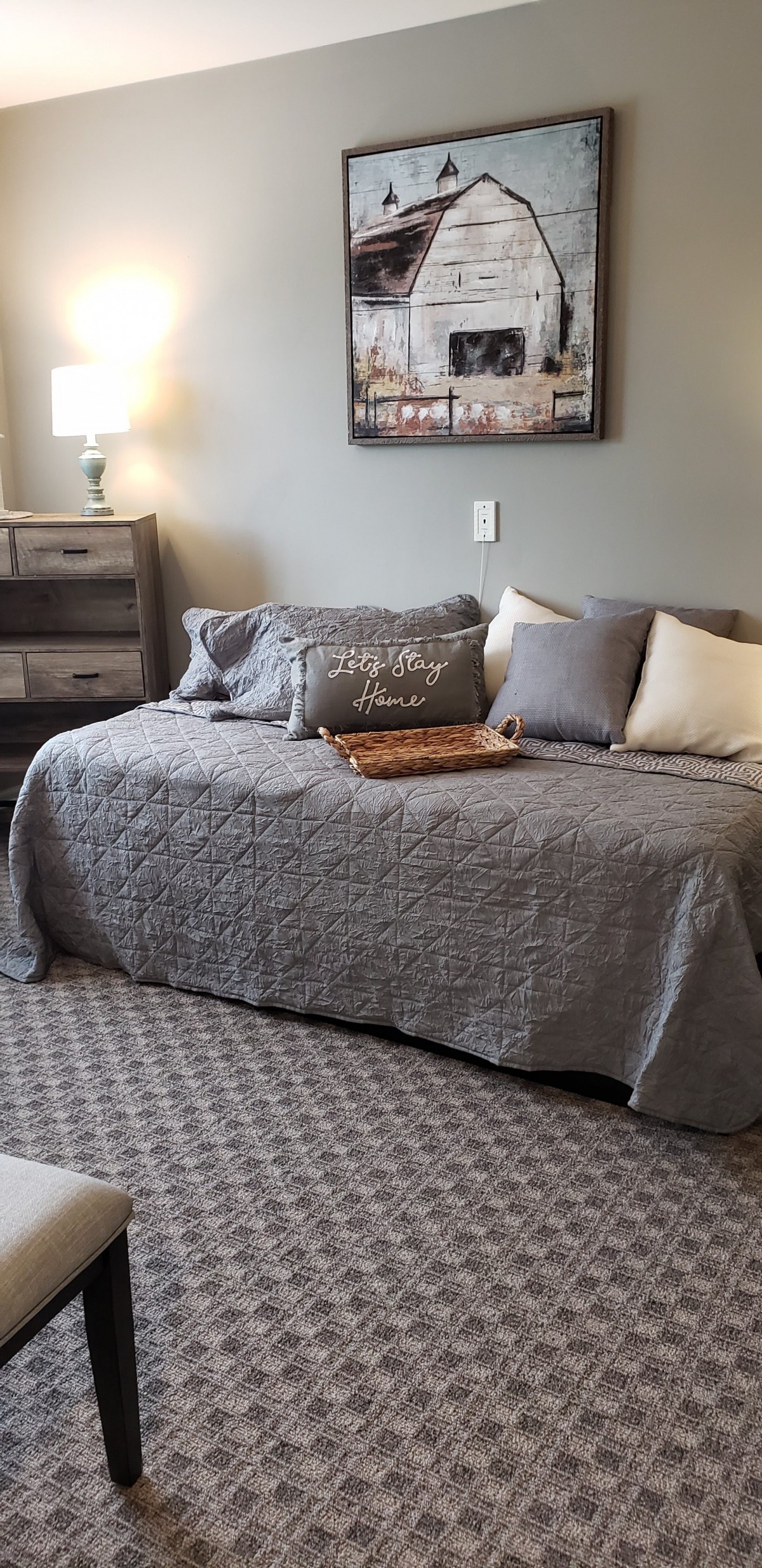 A cozy bedroom with a daybed adorned with gray bedding and pillows, complemented by a patterned rug and wooden bedside furniture.