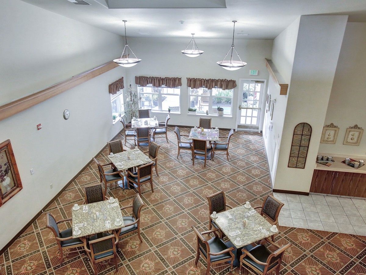 A spacious dining room with multiple tables and chairs, featuring large windows and overhead lighting.