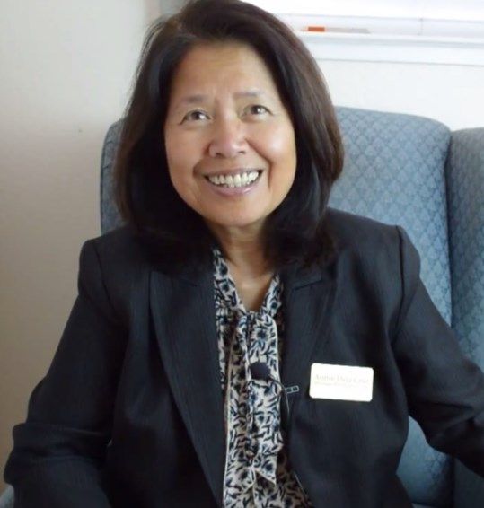 A woman in business attire smiles while sitting indoors.