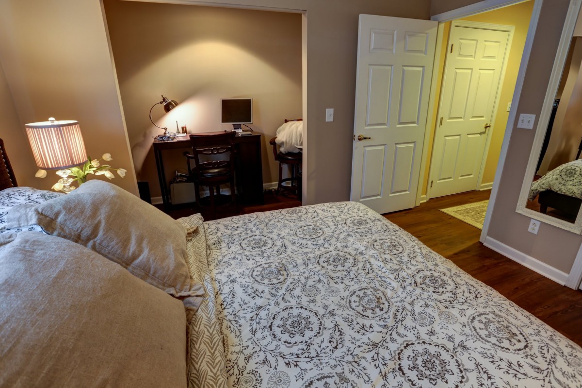 A cozy bedroom featuring a comfortable bed and a small workspace with a computer.