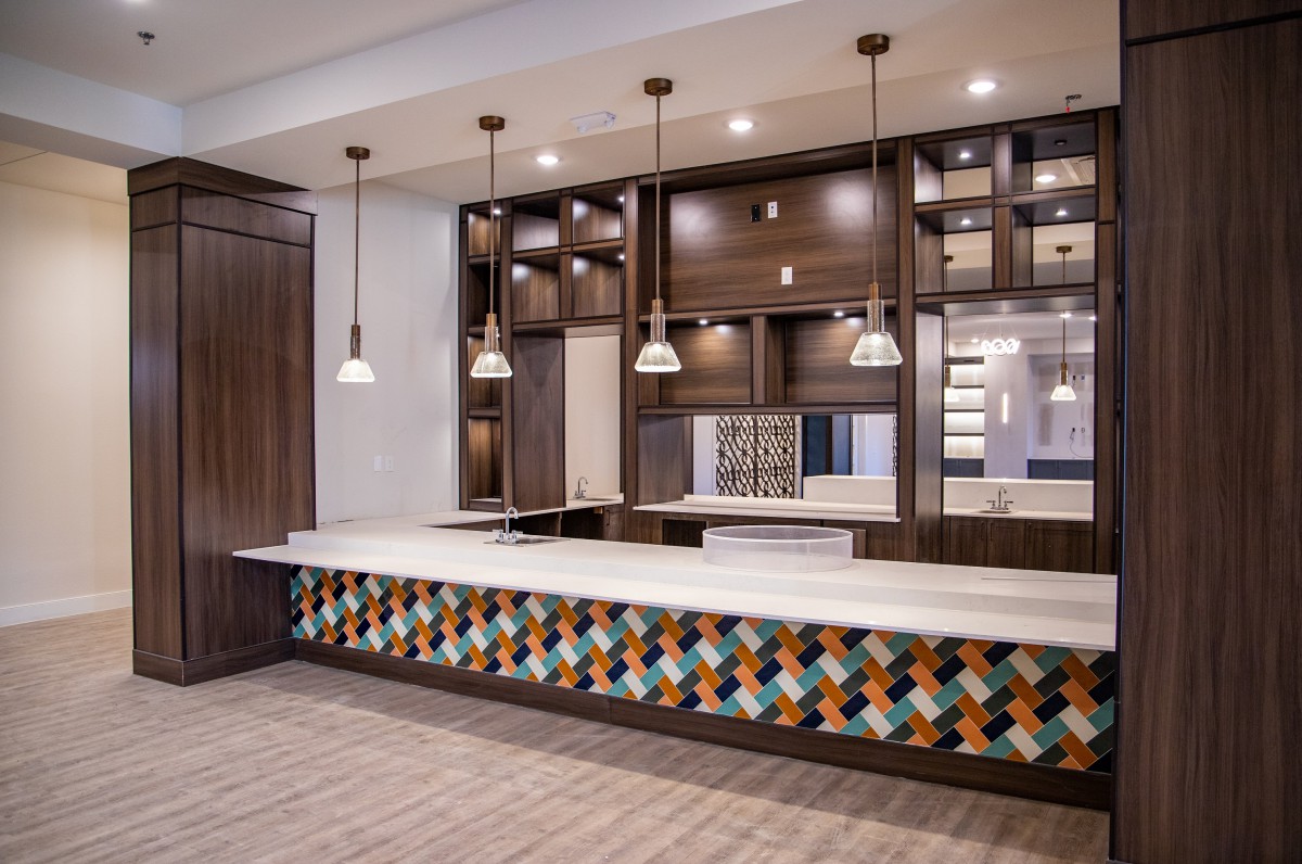 A modern kitchen interior featuring pendant lights, wooden cabinetry, and a vibrant patterned backsplash.