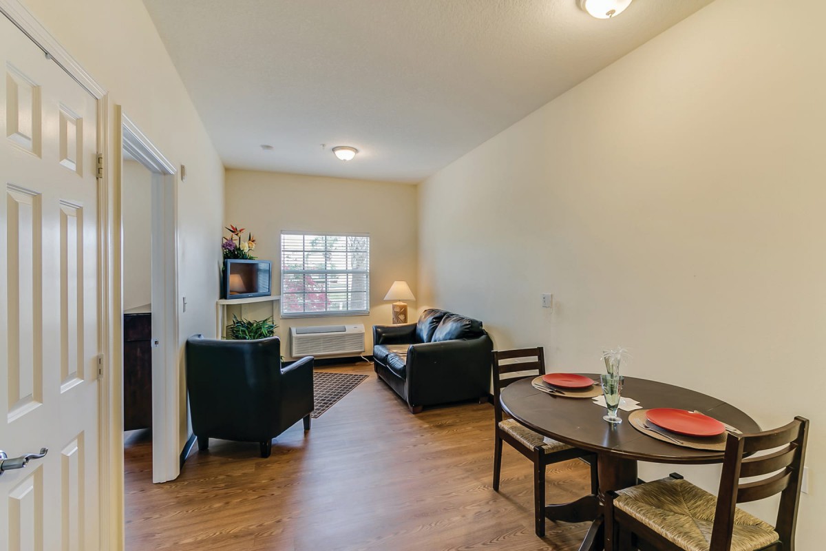 A cozy apartment living room with a dining area, featuring a sofa, chairs, and a table under soft lighting.