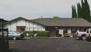 A small motel with a parking area and outdoor chairs.