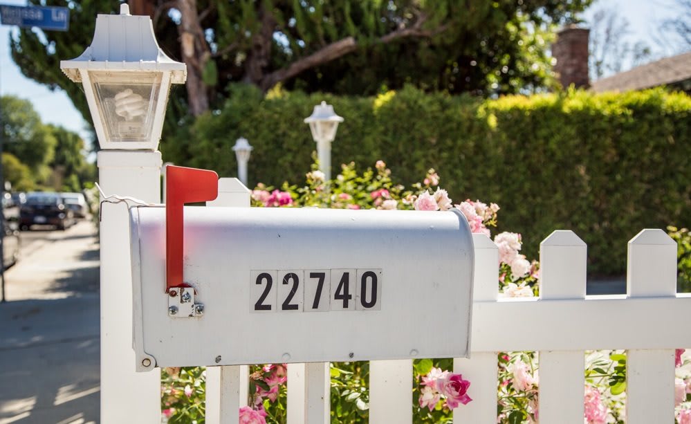 A silver mailbox with the house number 22740, surrounded by a white picket fence and garden flowers.