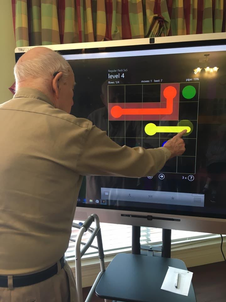 An elderly person using a touchscreen to play a puzzle game.