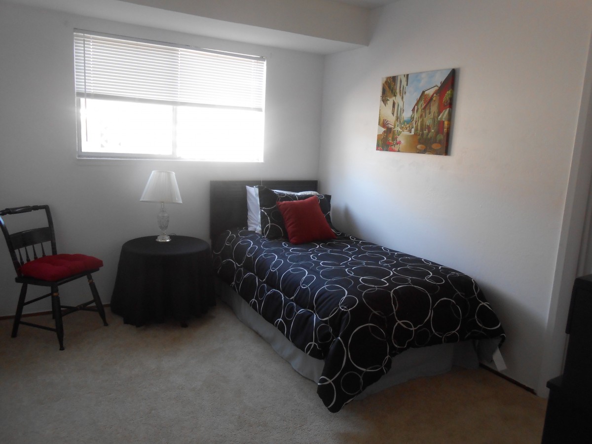 A small bedroom with a single bed, featuring decorative pillows and artwork on the wall.