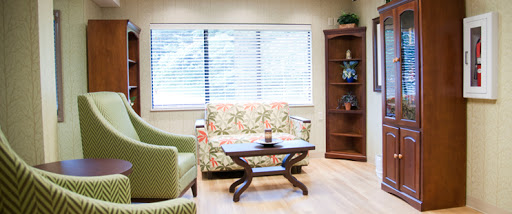 A cozy living room setup featuring a colorful floral sofa, a green armchair, and a wooden table by the window.