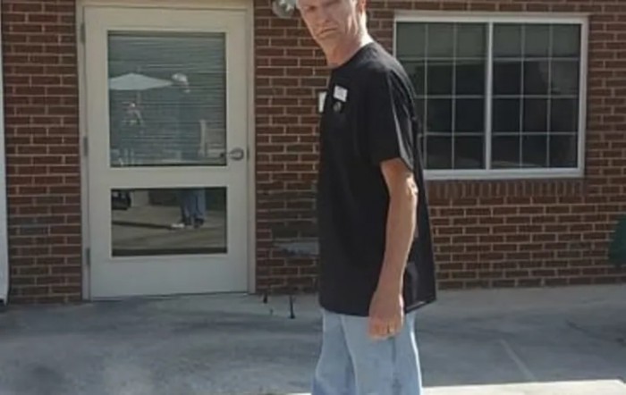 A man standing outside near a building, dressed in a black t-shirt and light shorts.